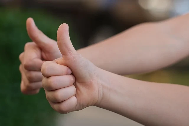 Two hands giving a thumbs up gesture against a blurred green background.
