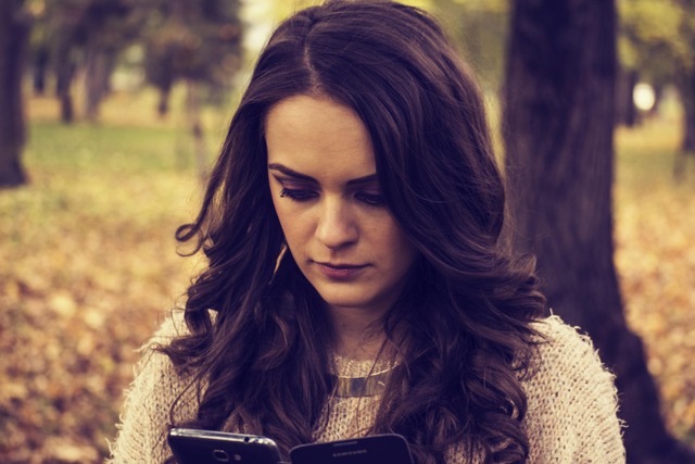A young woman holding and comparing two smartphones outdoors