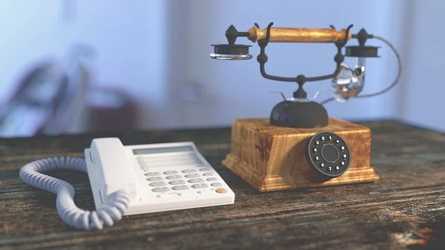 An old rotary phone and a modern push-button phone side by side.