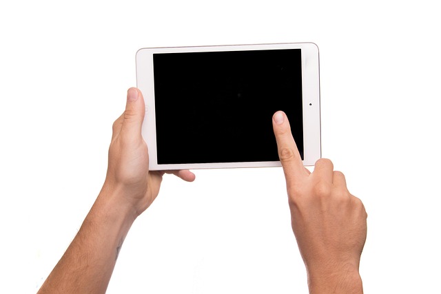 Hands holding a tablet with a finger touching the blank screen