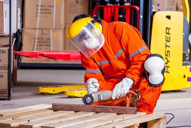 Worker in safety gear grinding metal in a warehouse setting
