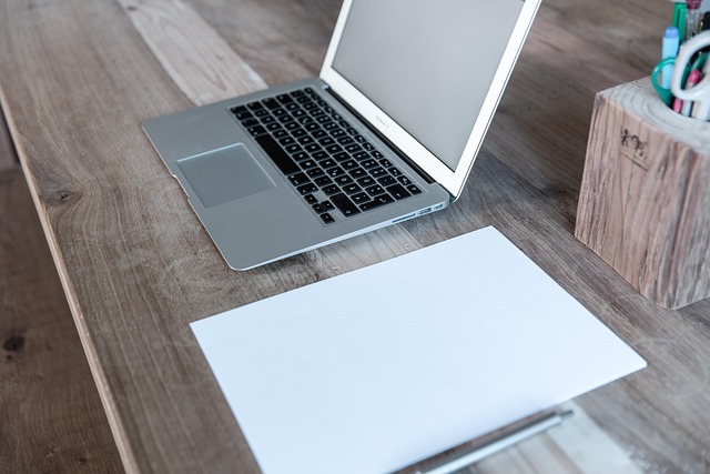 An open laptop and blank paper on a wooden desk