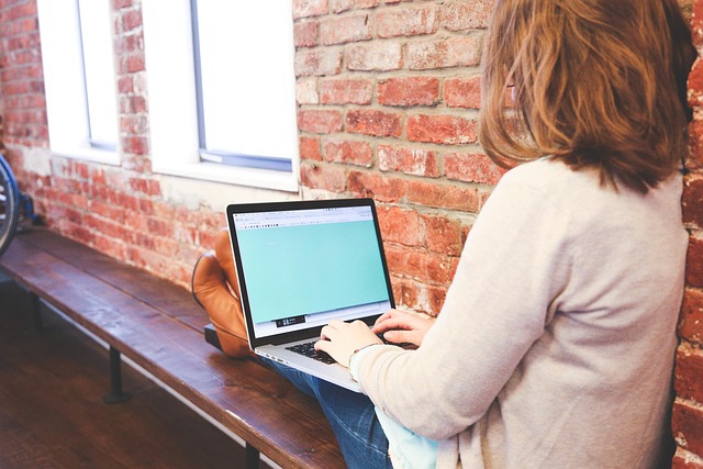 A woman using a laptop against an exposed brick wall