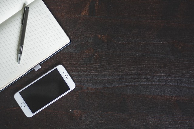 A white smartphone, notebook, and pen on a dark table