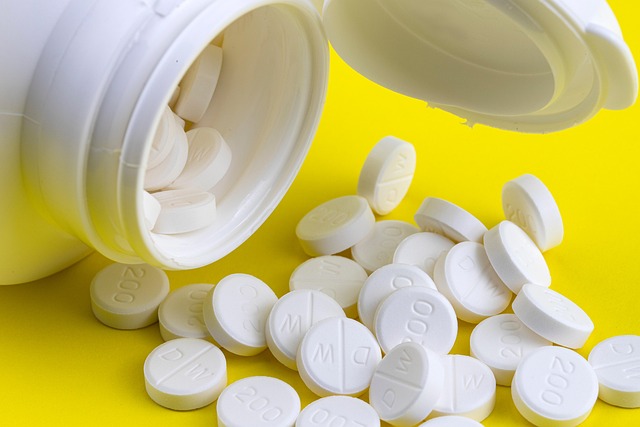 White pills spilling out of a pill bottle on a yellow background