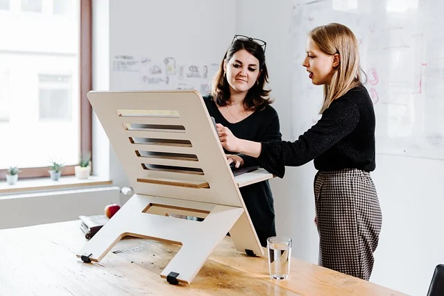 Remote work setup: Two women using a standing desk converter for ergonomic remote work.