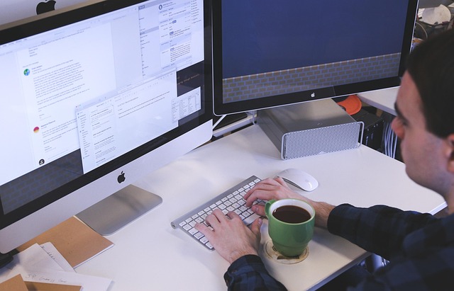 A developer typing on a keyboard in front of dual monitors