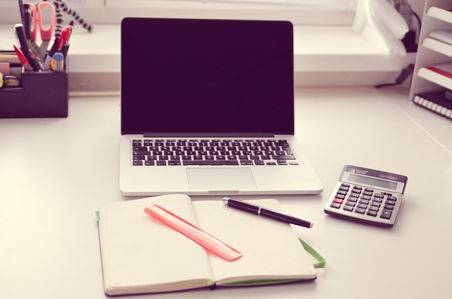 A laptop, notebook, pen, and calculator on a desk