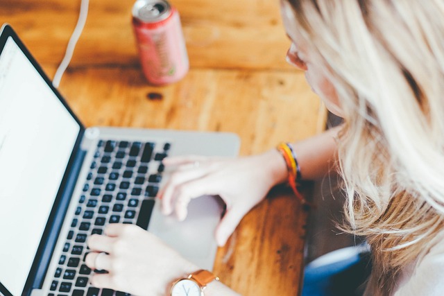 A woman typing on a laptop at a wooden desk