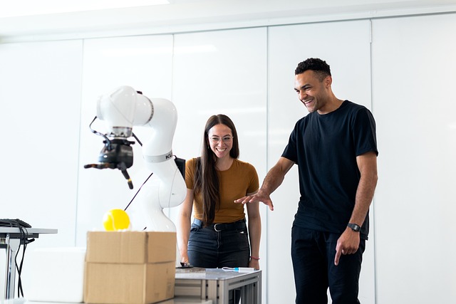 Two researchers watching a robotic arm pick up a tennis ball