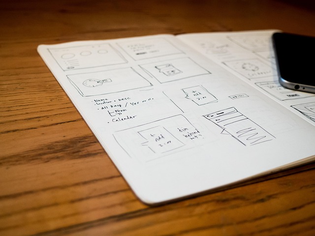 Hand-drawn mobile app wireframes in a notebook next to a smartphone