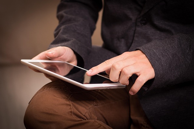 A person holding and touching a white tablet computer