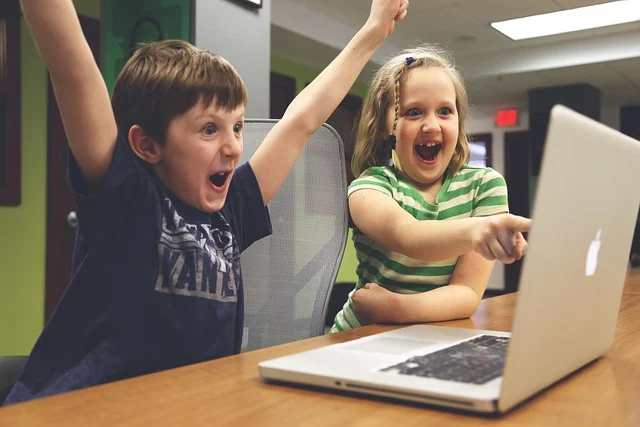 Two excited children looking at a laptop screen, one pointing.