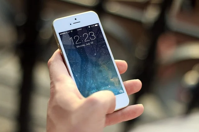 A hand holding an iPhone with a lock screen displaying time and date.