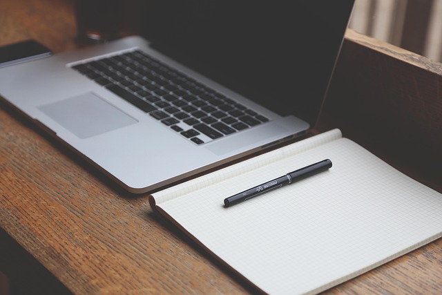 A laptop computer on a desk next to a notebook and pen