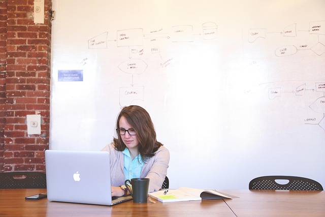 A woman working on a laptop near a whiteboard with diagrams