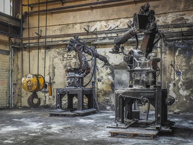 Two old industrial robots in a dirty, abandoned factory setting.