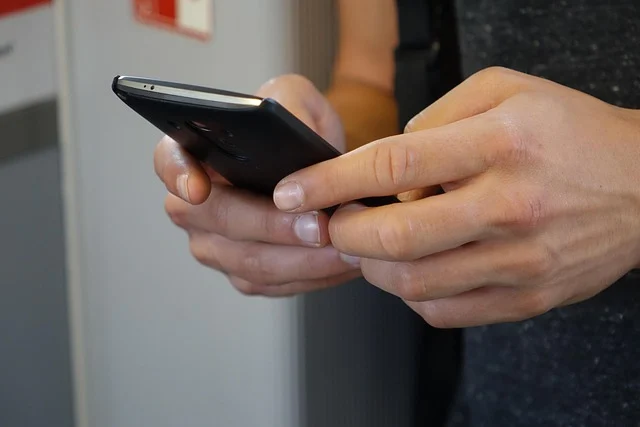 A person holding and using a black smartphone with both hands