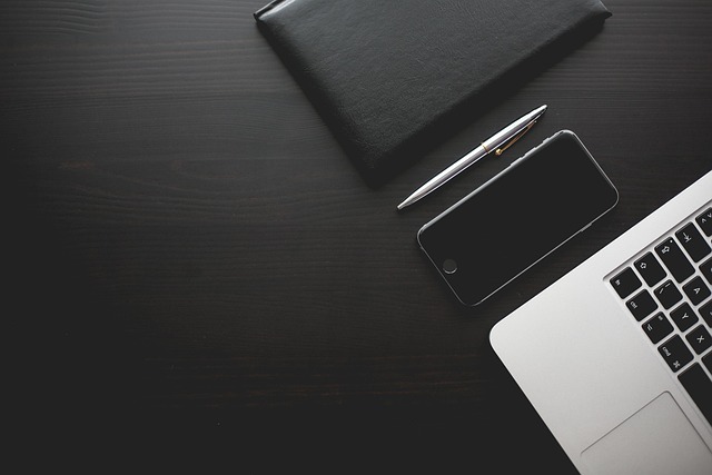 A desk setup with a smartphone, pen, notebook, and laptop
