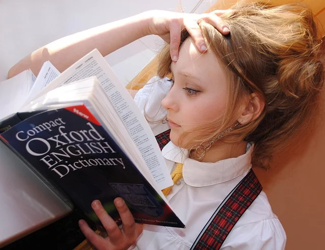 A young girl looking stressed while reading an English dictionary.