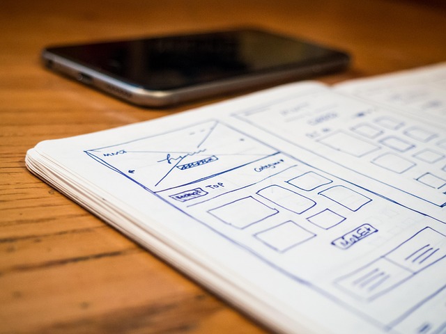 Hand-drawn mobile app wireframes in a notebook next to a smartphone
