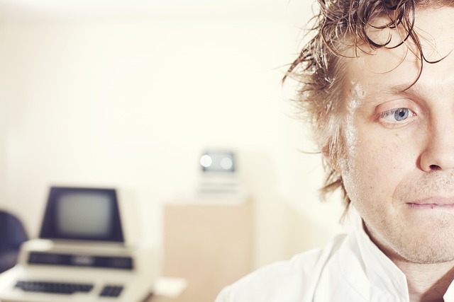 A close-up of a sweaty, worried man with vintage computer equipment