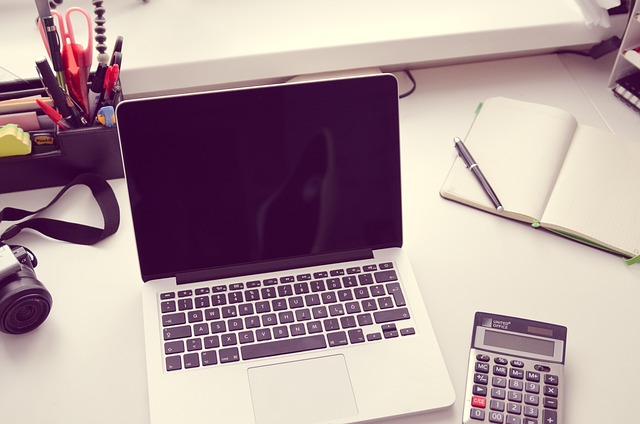 An open laptop, calculator, and notebook on a desk