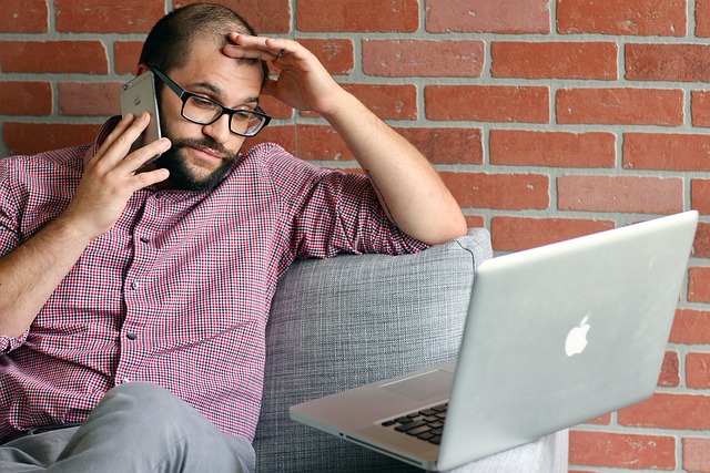 A frustrated man looking at a laptop while on the phone
