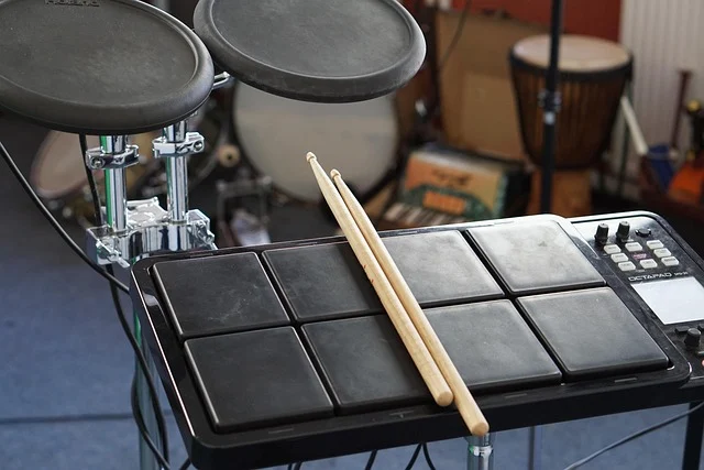 Electronic drum pads with drumsticks, cymbals, and other instruments in background