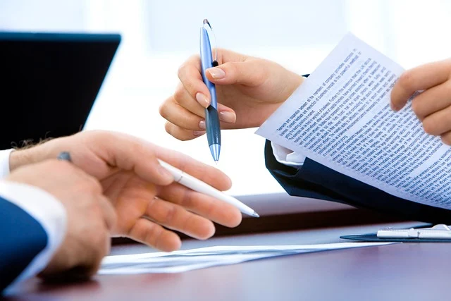 Firebase App Development Company: Two people discussing a document with pens, suggesting a business meeting.