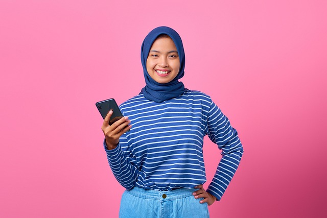 A smiling woman wearing a hijab holding a smartphone