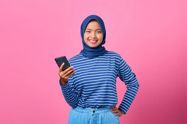 A smiling woman wearing a hijab holding a smartphone