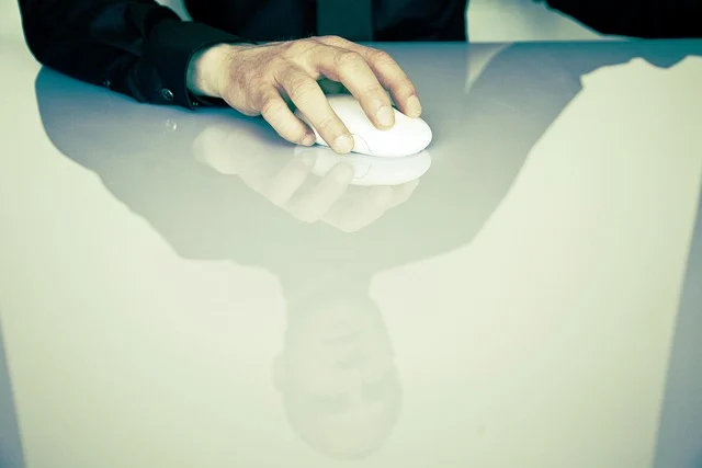 A person's hand using a computer mouse, with a reflection below.