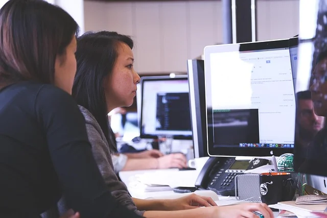 Two women working on computers in an office setting.