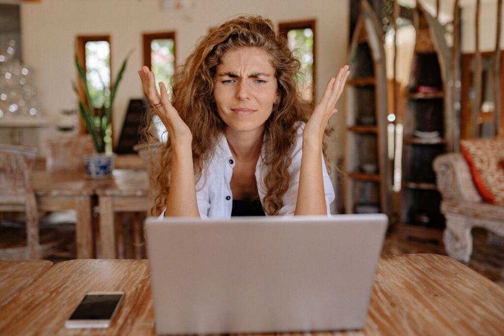 A frustrated woman looking at a laptop screen with raised hands