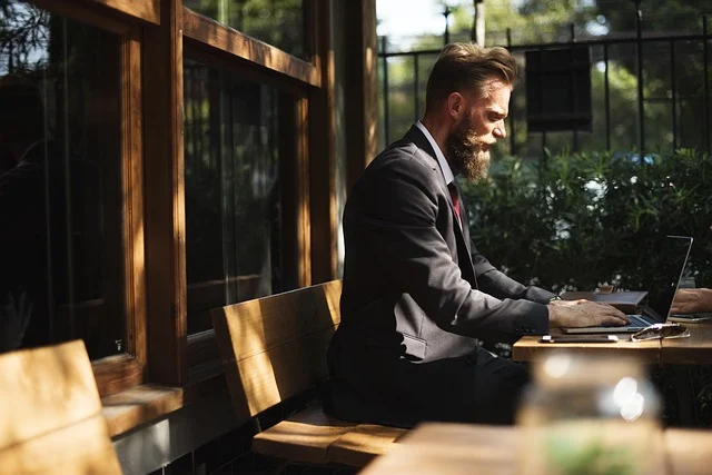 A bearded man in a suit working on a laptop outdoors