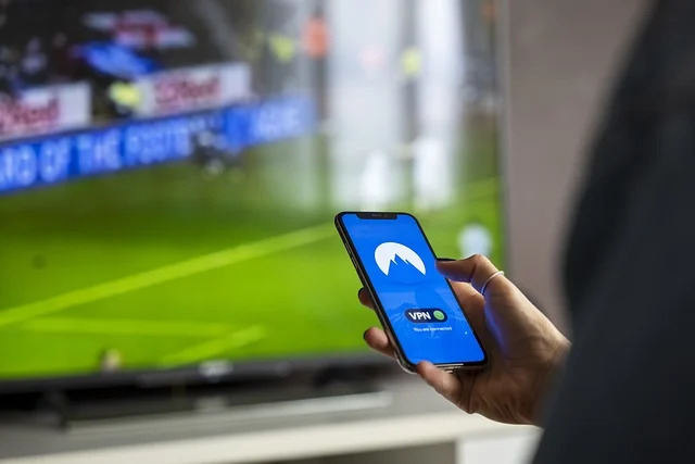 A person holding a phone with a VPN app, watching sports on TV.