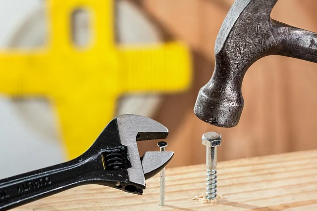 A wrench holding a nail and a hammer hitting a screw.