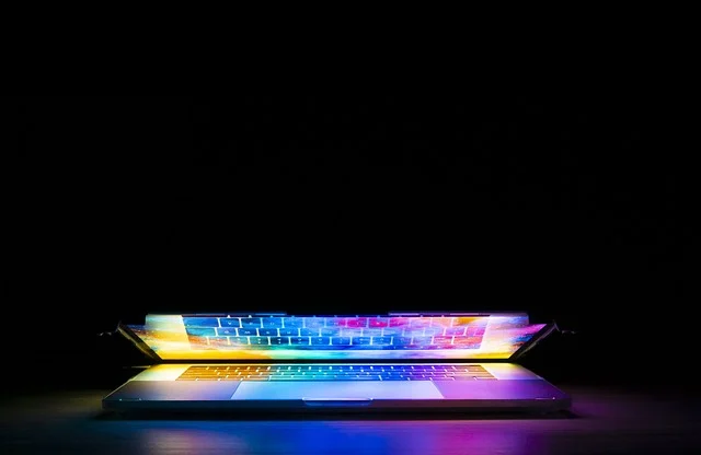 A laptop with a colorful, glowing keyboard and screen in a dark room.