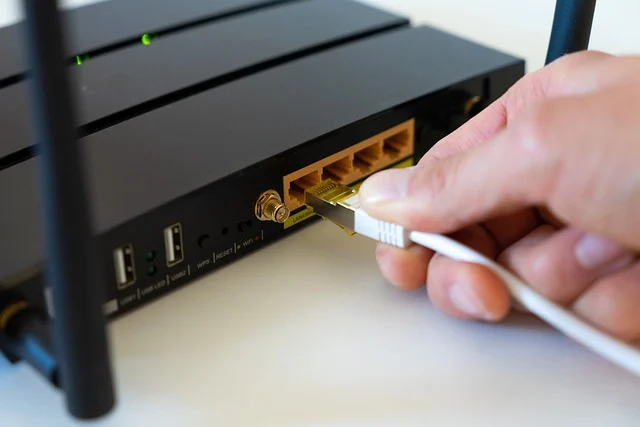 A hand plugging an Ethernet cable into a Wi-Fi router
