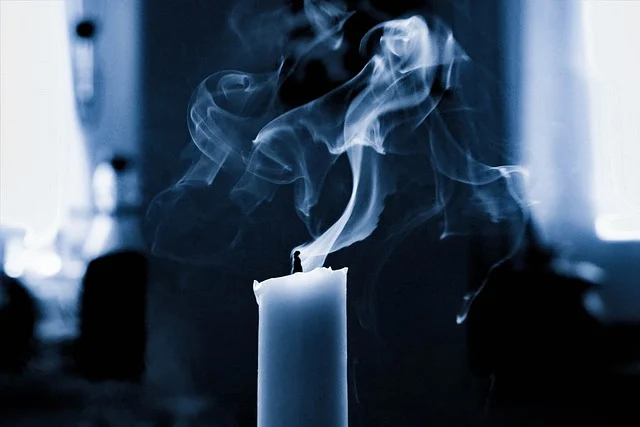 A candle with smoke rising, in a dark and overexposed setting.