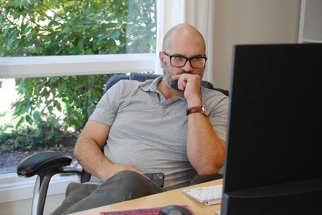 A man looking thoughtfully at a computer screen, possibly making a decision.