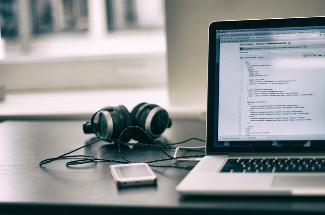 A laptop showing code next to headphones and a phone