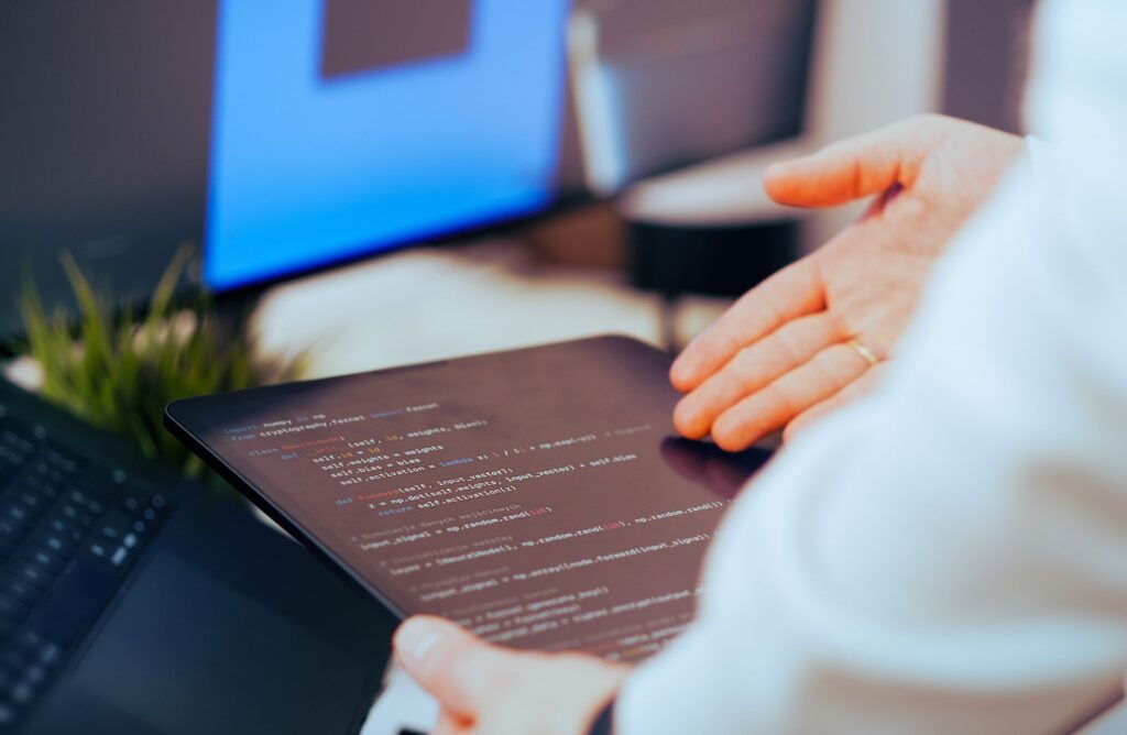 A person holding a tablet displaying code near a desktop computer