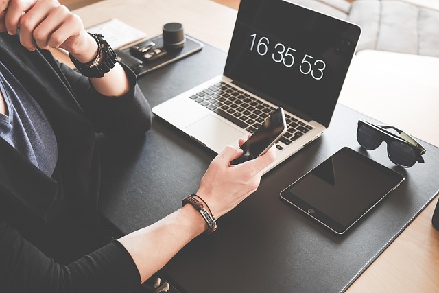 A person holding a smartphone near a laptop and tablet on desk