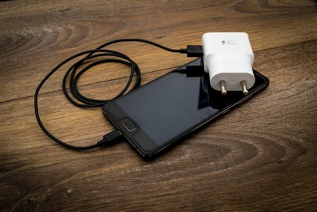 A smartphone charging with a wall adapter on a wooden surface.