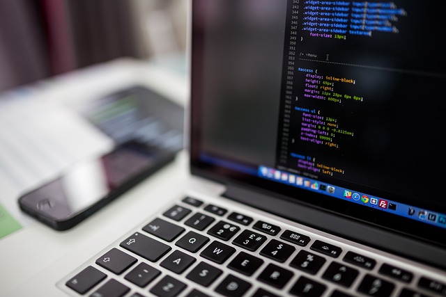 A laptop screen displaying code next to a smartphone on a desk