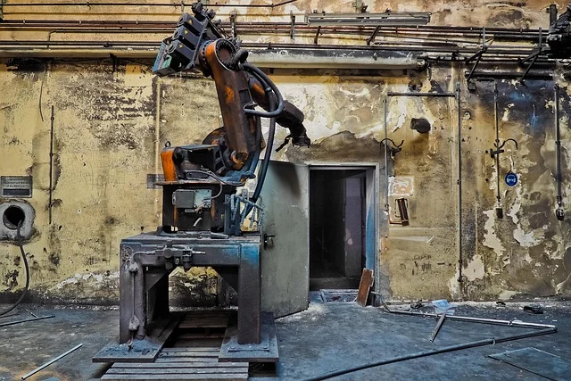 An old, rusty industrial robot in a dilapidated factory setting.