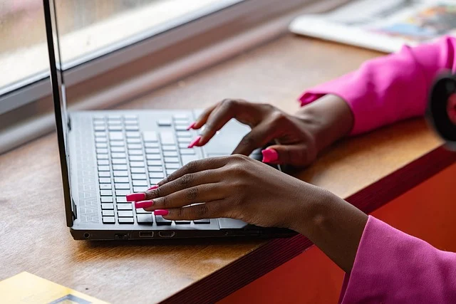 A person's hands typing on a laptop keyboard, with bright pink nails.