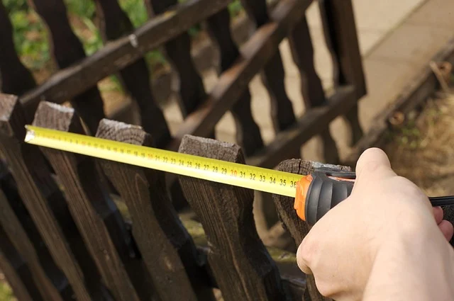 Golang compare: A person measuring a wooden fence with a yellow tape measure